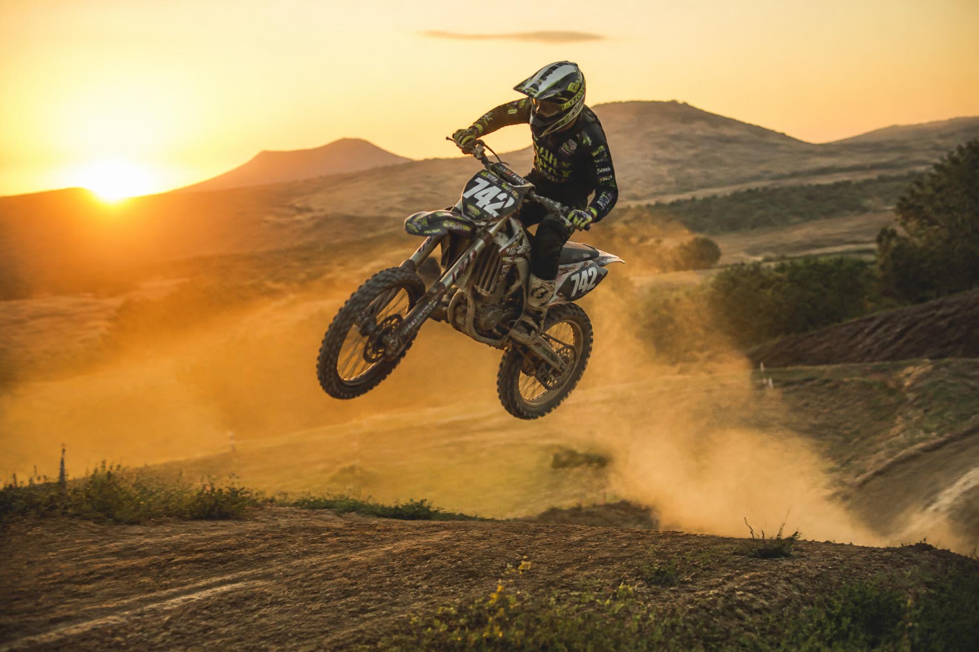 Pilota motocross in volo su pista sterrata al tramonto